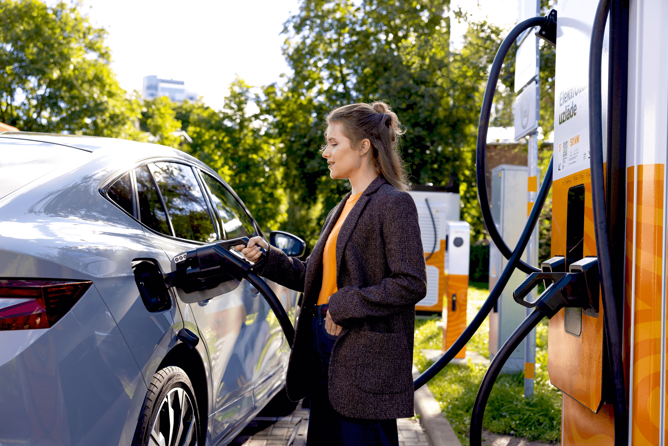 Sieviete pieslēdz elektroauto pie Elektrum Drive ātrās uzlādes stacijas.