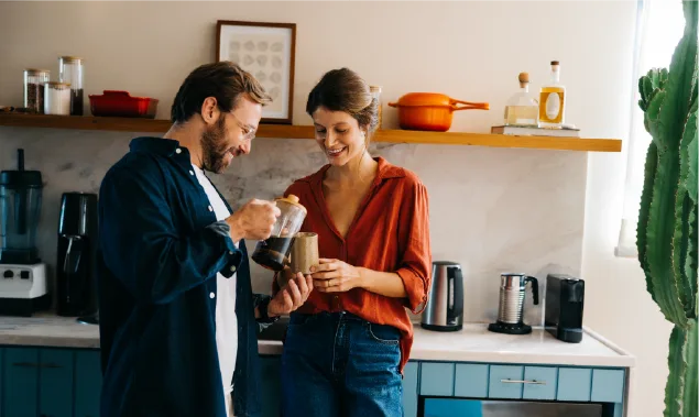 A man and a woman are standing in the kitchen, drinking coffee.