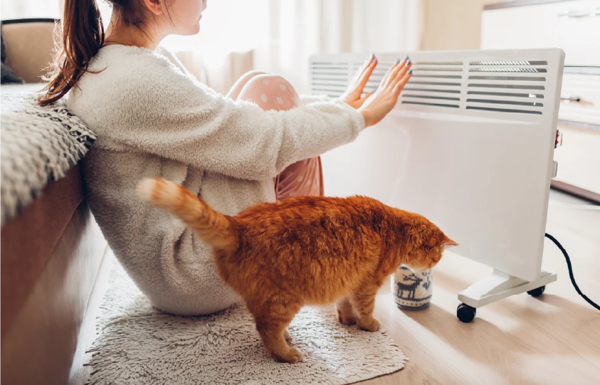 Meitene sēž blakus elektriskajam radiatoram un silda plaukstas