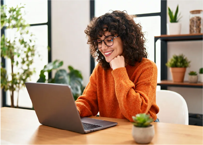 A woman is sitting at a table and carefully looking at a laptop screen.