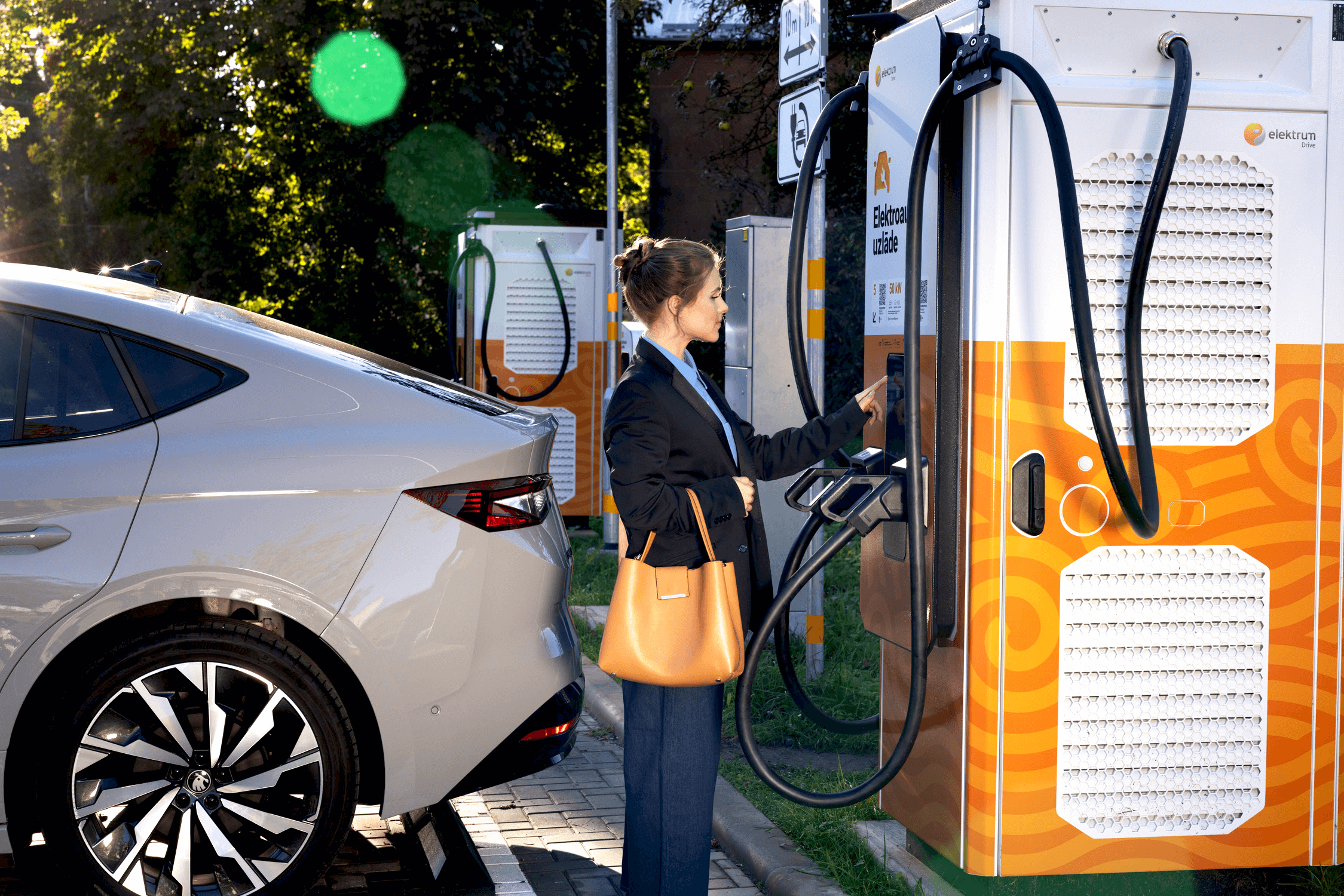 A woman is standing next to an Elektrum Drive fast-charging station and activating it.