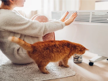 Meitene sēž blakus elektriskajam radiatoram un silda plaukstas